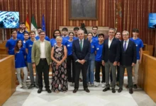 Grupo de estudiantes y representantes institucionales en el Salón Colón del Ayuntamiento de Sevilla durante un encuentro universitario.