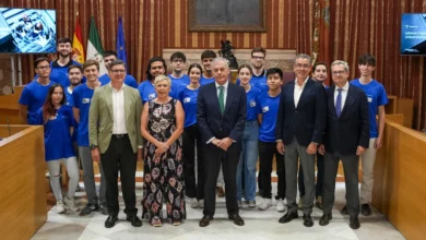 Grupo de estudiantes y representantes institucionales en el Salón Colón del Ayuntamiento de Sevilla durante un encuentro universitario.