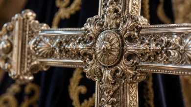 Primer plano de una cruz procesional de metal ornamentado junto a un tejido ceremonial, con el fondo desenfocado.