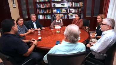 Reunión de varias personas alrededor de una mesa en una oficina con estanterías de libros al fondo.