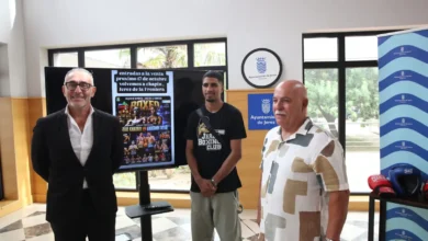 Tres hombres posan en una sala junto a una pantalla con el cartel de una velada de boxeo y material deportivo sobre una mesa.