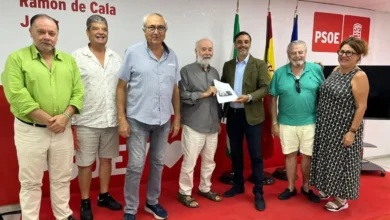 Grupo de siete personas en una sala con imagen corporativa del PSOE, banderas y una persona sosteniendo un documento.