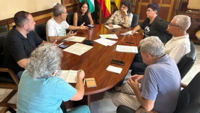 Varias personas reunidas alrededor de una mesa en una sala municipal de Sanlúcar, con banderas de Andalucía y España al fondo