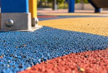 Primer plano de un pavimento continuo de caucho de colores junto a la base metálica de un juego infantil.