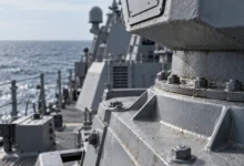 Primer plano de una estructura naval de acero gris con pernos metálicos, juntas y detalles de superficie junto al mar.