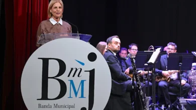 Mujer ante un atril durante la presentación de la Banda Municipal de Música de Jerez, con varios músicos al fondo y el logotipo de la formación en primer plano.