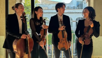 Cuatro intérpretes de cuerda posan juntos junto a sus instrumentos en un espacio interior