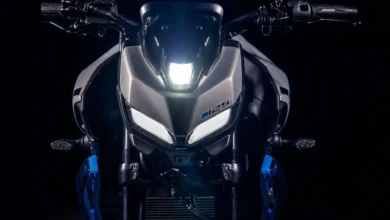 Vista frontal de una motocicleta Yamaha MT-125 con iluminación blanca encendida, carrocería gris, detalles azules y fondo negro.