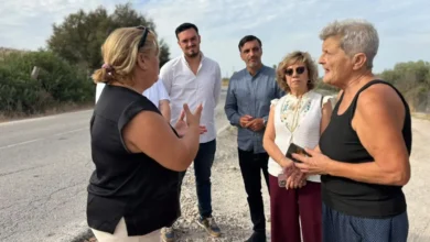 Cinco personas conversan junto a una carretera con vegetación y un arcén de grava