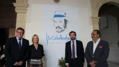Cuatro personas posan ante un cartel dedicado a José Manuel Caballero Bonald en un espacio interior.